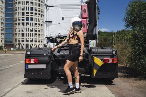 A beautiful Caucasian female wearing a helmet and posing in the back of a truck on a sunny day