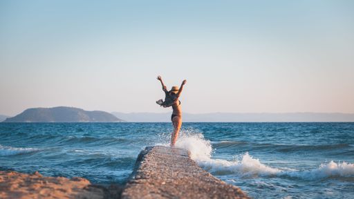 A beautiful woman standing on a rock with her hands in the air in a beach