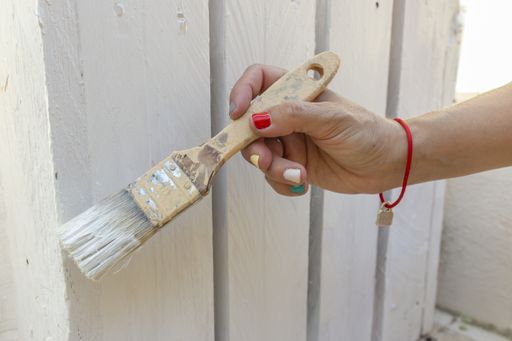 The hand of a female painting and reforming a wooden fence