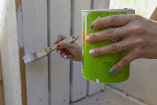 A selective focus shot of a women hand holding a metal paint can and painting a fence