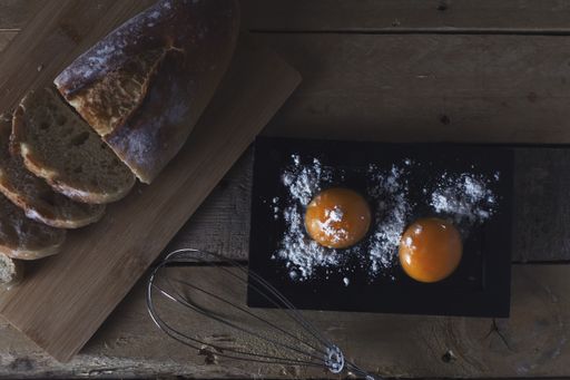 An overhead shot of two egg yolks with flour and a few slices of cut bread on a wooden table