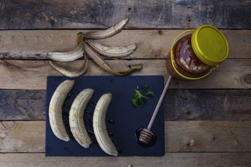 A flat lay of a black slate board with bananas covered with honey, and honey dipper