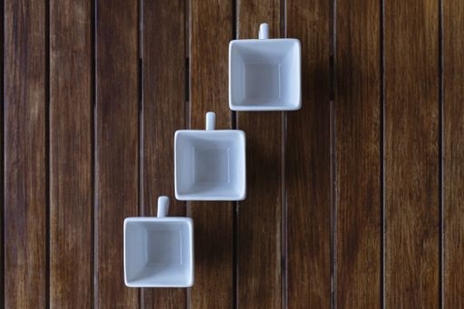 A high angle shot of three white square cups on a wooden surface