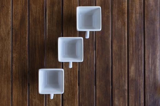 A high angle shot of three white square cups on a wooden surface