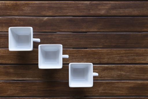 A high angle shot of three white square cups on a wooden surface
