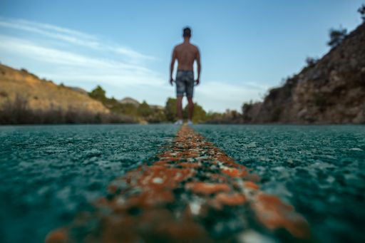 A low angle show of a shirtless male walking down along the center of a highway