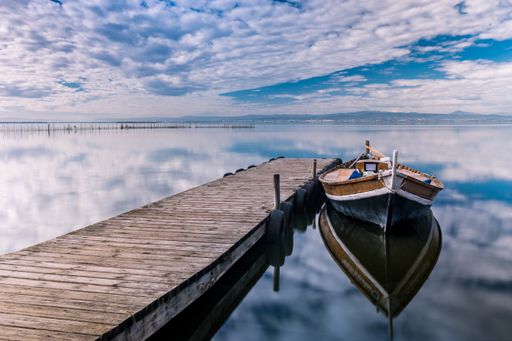 A boat parked near the wooden pier with reflections in the sea under the cloudy sky