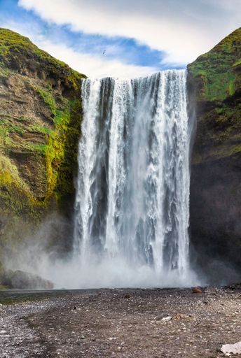 A vertical shot of Seljalandsfoss waterfall against a cloudy sky in Iceland