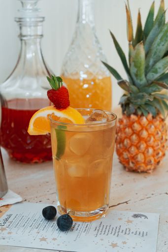 A vertical closeup shot glass with fresh liquid on a table with fruits and glass bottles