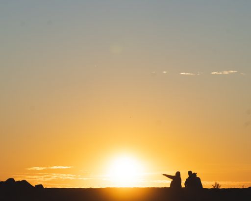 A horizontal shot of two people in silhouette sitting on the ground during sunset. Perfect for a travel blog
