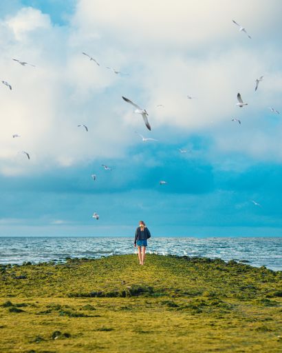 A beautiful vertical shot of a woman in a skirt standing in a green field near a body of water.