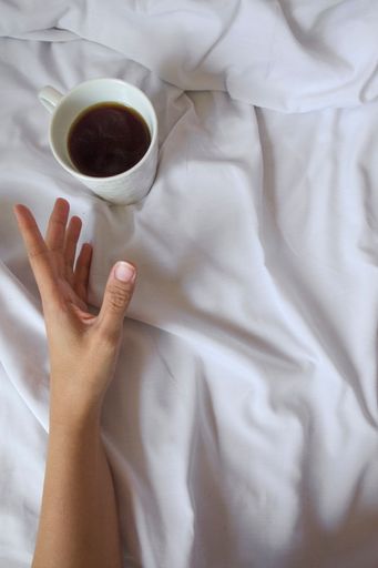 Hand stretched towards a cup of coffee screaming for awakening.