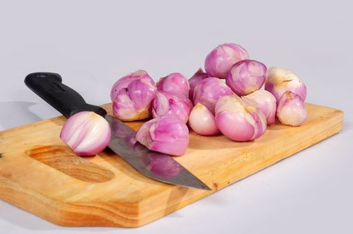 An isolated view of peeled shallots on the wooden cutting board on an empty background