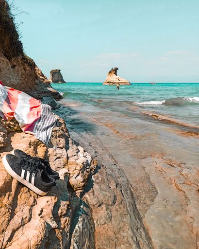 A vertical shot of sneakers near the beach with a blue sea in the background