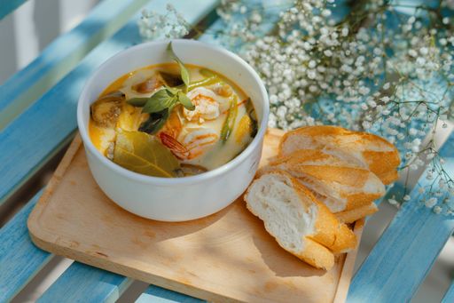 A high angle closeup shot of a soup with seafood and vegetables with baguette slices on a blue bench