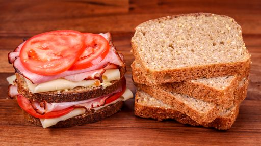 A ham sandwich with cheese and tomato and stack of bread slices on wooden table