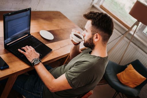 A young male drinking coffee while working on a laptop at home