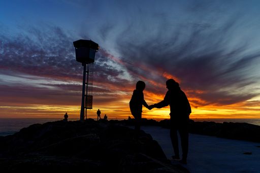 A silhouette shot of a father and his child in front of a lighthouse under the beautiful sky during sunset