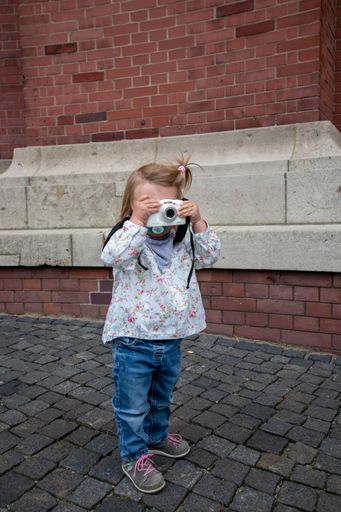 A vertical shot of a cute girl shooting by a white camera standing on tiled stone floor
