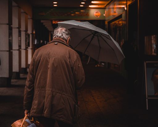 A closeup of an old man seen from behind, holding an umbrella, walking in Vienna, Austria