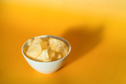 A high angle shot of plain potato chips in a white glass bowl on a yellow background