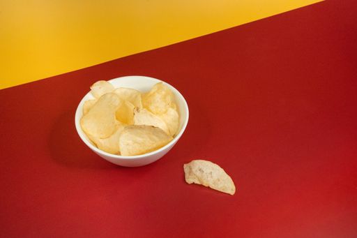 A high angle shot of plain potato chips in a white glass bowl on a yellow red background