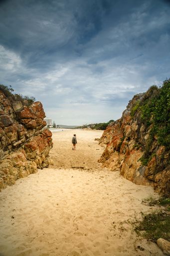 A vertical rear view of a girl standing between two rocks on the beach in South Africa