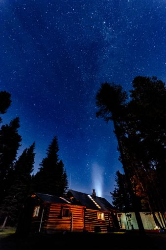 A low angle shot of wooden cabin in Flathead National Forest near Glacier National Park against starry sky background