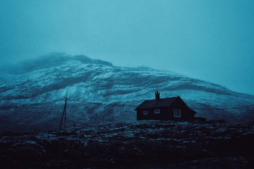A beautiful shot of a house on a hill with an amazing mountain in the background covered in fog