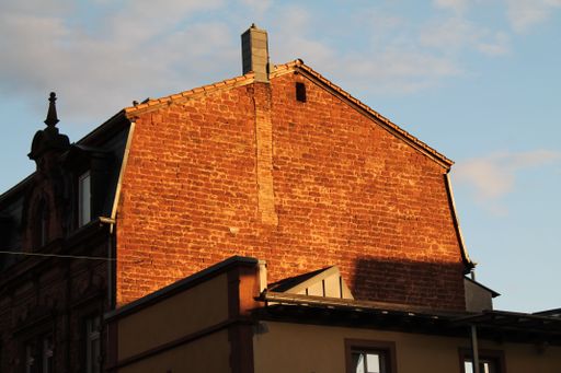 An old red brick building with a chimney against a cloudy sky on a sunny day