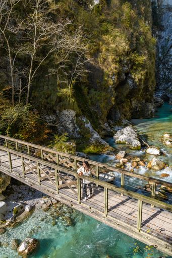 A high angle shot of a female on a wooden bridge on a river in Tolmin Gorges, Slovenia