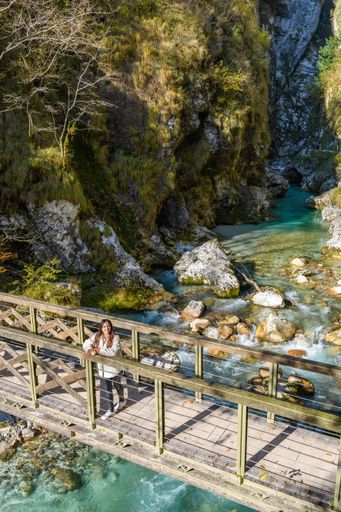 A high angle shot of a female on a wooden bridge on a river in Tolmin Gorges, Slovenia