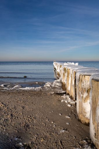 A vertical shot of a wooden pier covered in snow in a sandy beach  during wintertime