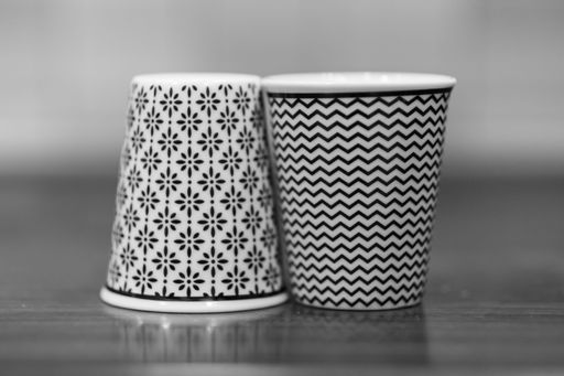 A black and white shot of two plastic cups with decorations on a wooden table