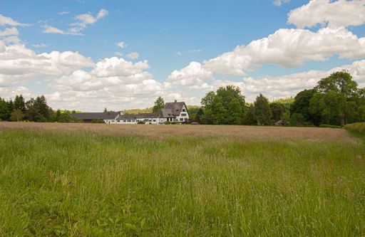 A scenic view of a farm in green agricultural lands under a cloudy blue sky