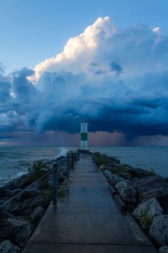 A vertical shot of a white lighthouse on the sea shore with a cloudy sky on the background