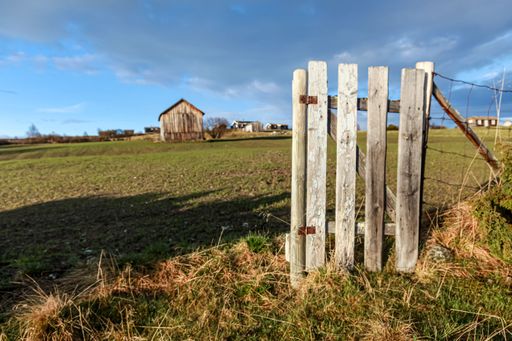 An old wooden fence in a rural area with a small hut in the background in sunny weather