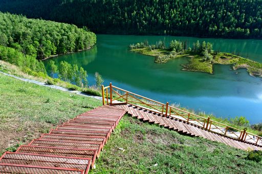A horizontal shot of the beautiful Kanas lake surrounded by green trees and red staircases in China