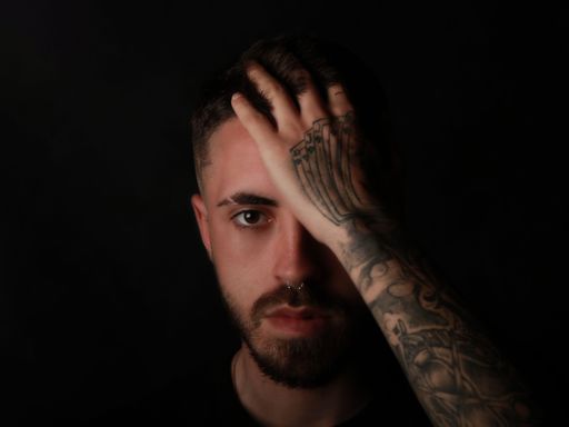A closeup shot of a Caucasian man with tattoos against the black background