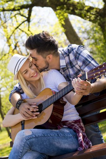 A happy caucasian couple sitting on a park bench with a guitar