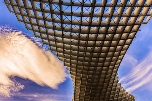 A low angle shot of a modern design ceiling of a building against a cloudy blue sky