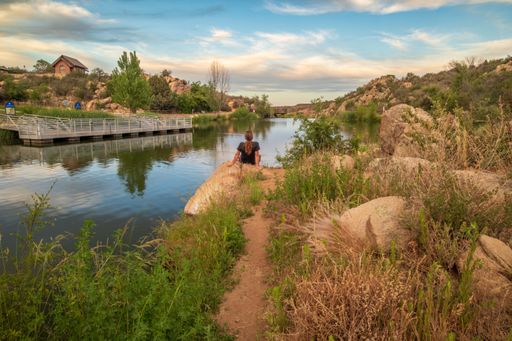 A scenic view of a male seen from behind, sitting on a bank of Fain Lake in Prescott Valley, Arizona at sunset