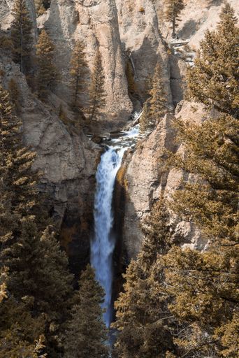 A high angle shot of a waterfall flowing down the rocks covered with green trees on a sunny day