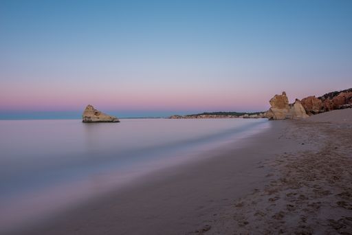 A horizontal shot of a beautiful beach and the blue sea surrounded by rocky hills under the colorful sky in Algarve, Portugal