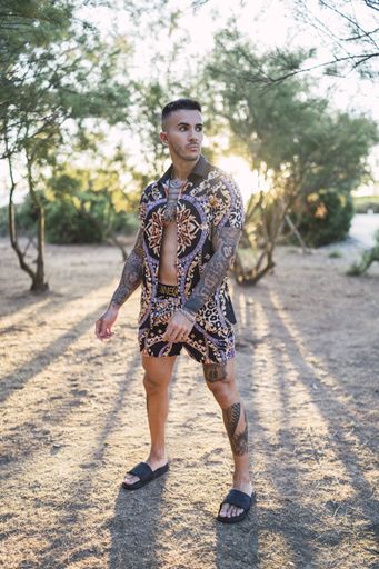 A vertical shot of a Caucasian male with tattoos wearing fashionable clothes posing at the beach