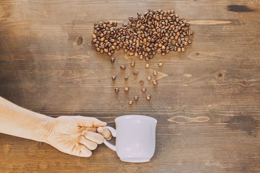 A high angle shot of a cup of coffee near coffee beans on a wooden table
