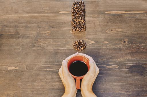 A high angle shot of a cup of coffee near coffee beans on a wooden table