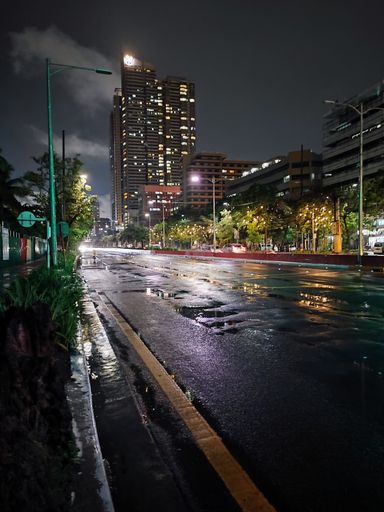 A vertical shot of high rise buildings and street lamps in a wet street at night in Manila