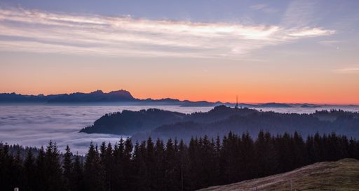 A view of a scenic red sunset over a rural area with a lot of trees and hills covered with fog