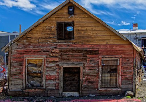 An old red and brown wooden hut with a triangle roof against blue sky background